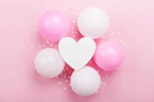 Birthday or wedding mockup with white heart shape, confetti and pastel balloons on pink table top view. Flat lay composition.