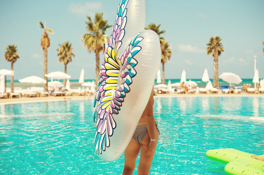 Sexy woman holding inflated buttfly float in front of blue swimming pool