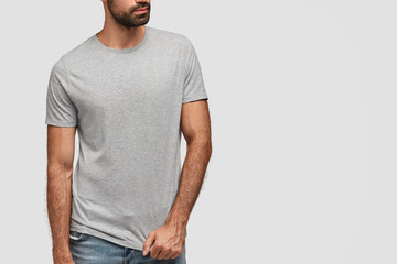 Unrecognizable bearded muscular guy wears gray casual t shirt with blank copy space for your...