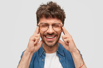 Negative human emotions and feelings concept. Desperate Caucasian young male frowns face, keeps index fingers on temples, makes decision, feels pain, closes eyes, isolated over white background