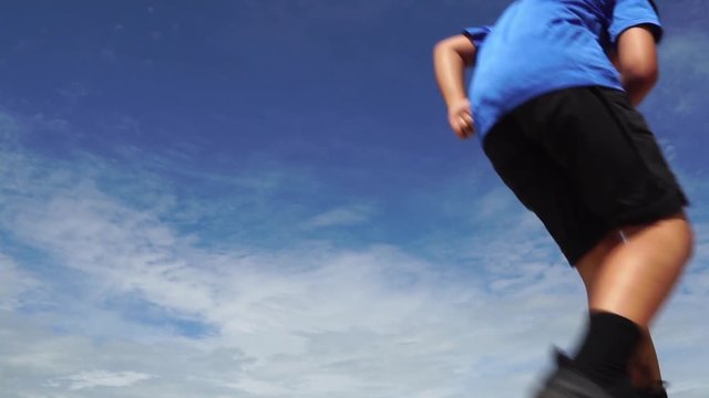 Slow motion oung boy run and jump over a weeds during blue sky in summer.