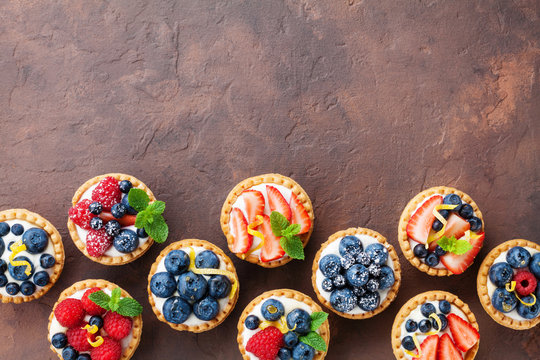 Delicious berry tartlets or cake with cream cheese decorated lemon peel and mint leaf from above. Tasty pastry desserts.