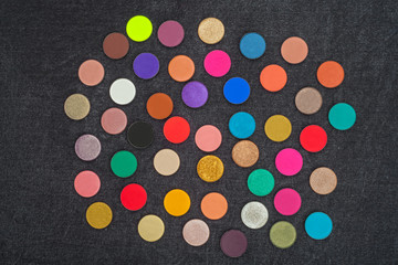 set of many shimmer and matt multicolored circle shaped eye shadows lying on a black background. concept of professional make up tools