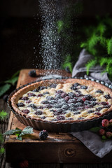Falling powdered sugar on blackberry pie on wooden table