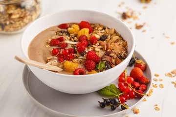 Smoothie bowl with banana, cocoa, berries and homemade granola, white background. Healthy vegan food concept.