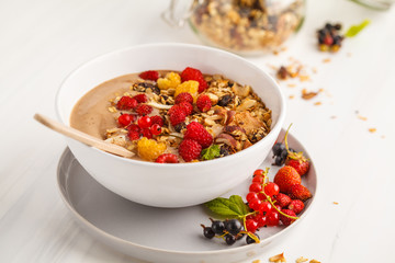 Smoothie bowl with banana, cocoa, berries and homemade granola, white background. Healthy vegan food concept.