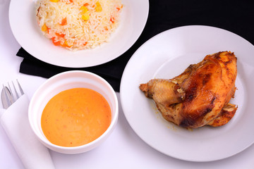 Grilled chicken on a white plate with sauce in a bowl and risotto flat lay