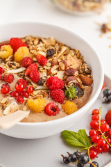 Smoothie bowl with banana, cocoa, berries and homemade granola, white background, vertical. Healthy vegan food concept.