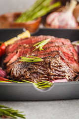 Sliced roast beef in a frying pan with spices and vegetables, white background, macro