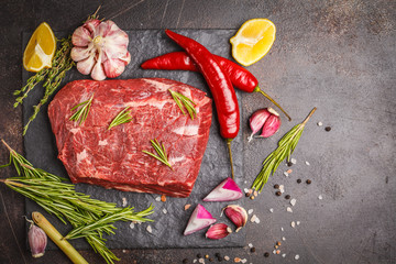 Raw whole piece of beef on slate with spices, top view.