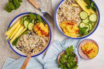 Vegan lunch with rice, hummus and vegetables in white plates, top view.