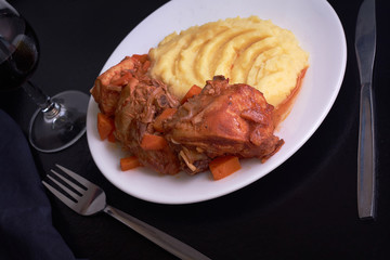 Cooked chicken under sauce with smashed potatoes and glass of wine on table with black table cloth