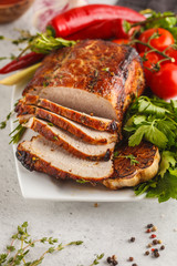 Roasted pork with thyme, rosemary, garlic and tomato sauce on a white dish, white background, vertical