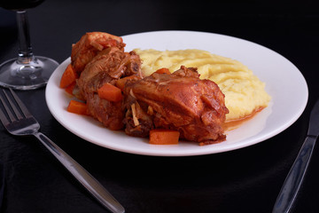 Cooked chicken under sauce with smashed potatoes and glass of wine on table with black table cloth