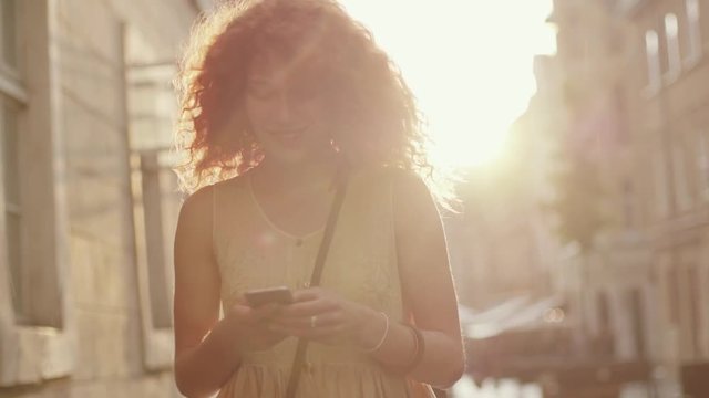 Portrait red haired young smiling woman walking in the city use phone in sunset streets smile happy slow motion summer face technology casual caucasian female beautiful lady outdoor closeup cute rain