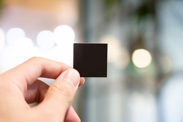 Hand holding blank black small paper with blury background.