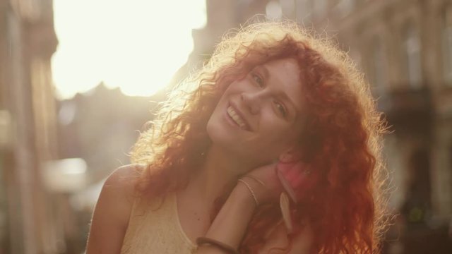 Close up face smiling woman with red curly hair look at camera smile walking in the city streets portrait happy slow motion summer face casual caucasian sunset lady outdoor closeup cute