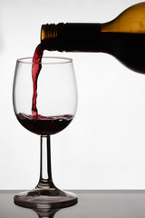 Close up of pouring of red dry wine in a crystal wine glass from full bottle of wine with splashes on a white isolated background