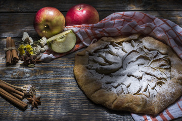 Homemade apple pie with powdered sugar, spices served with a textile towel on a wooden board, background. Top view