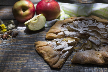 Homemade apple pie with powdered sugar, spices served with a textile towel on a wooden board,...