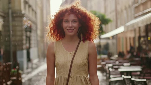 Happy smiling attractive woman with red curly hair walking in the rain on the street cute fashion water silhouette girl summer face female portrait slow motion lonely stop close up
