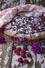 Fresh ripe juicy raspberries on baked pie with flowers on a wooden old background, decorated with a textile towel.