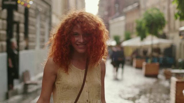 attractive woman with red curly hair walking in the rain on the street look at camera spinning happy smile cute fashion water silhouette summer face female lonely stop close up