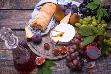 Crystal decanter with red wine and glass of wine with set of products - cheese, grapes, figs, plums, pears, white bread on wooden background.