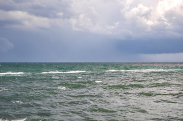 Small waves, on the Black Sea coast. The sun shines, there are small white clouds in the sky. Light breeze and excitement. In the distance, the horizon line is visible.