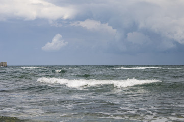 Coast of the Black Sea. Surf. Light breeze. Small waves, with white foam, from the water. The color of sulfur, black, blue.