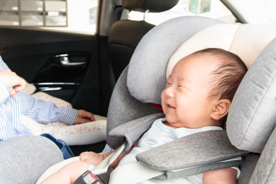 Asian Little Smiling Baby Child Fastened With Security Belt In Safety Car Seat