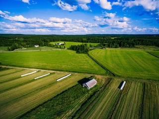 Aerial view of green field harvest with old wood barn and bales of hay in white plastic in rural...