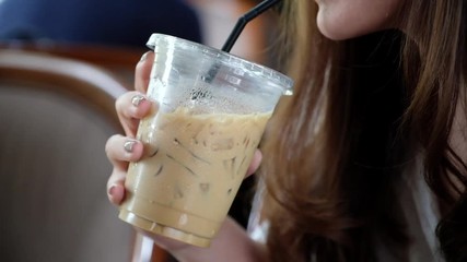 A woman holding and drinking iced coffee by straw in cafe
