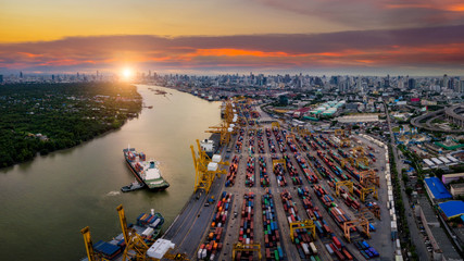 Aerial view of international port with Crane loading containers in import export business logistics with cityscape of Bangkok city Thailand at sunset