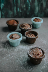 Appetizing chocolate brownie cupcakes sprinkled with powdered sugar in confectionery molds of brown and blue colors.
