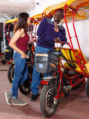 Fototapeta na wymiar Polite African-American bikecab driver talking to young woman, offering rickshaw service