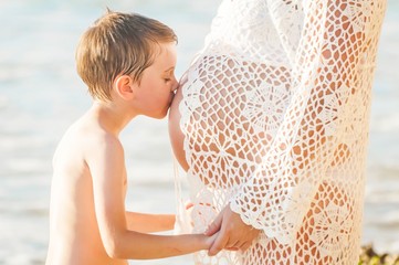 Cute Caucasian boy kissing his pregnant mother's belly. Unconditional love concept, expecting a...