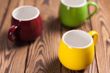 Three colored empty ceramic clean mugs on old worn brown wooden table