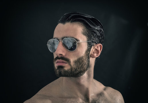 Handsome young man shirtless wearing sunglasses, on black background in studio shot