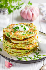Zucchini pancakes with parsley and sour cream, summer food, tasty snack. High stack in a plate on white wood