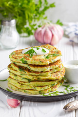 Zucchini pancakes with parsley and sour cream, summer food, tasty snack. High stack in a plate on...