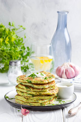 Zucchini pancakes with parsley and sour cream, summer food, tasty snack. High stack in a plate on white wood