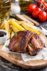 Grilled meat ribs with fried potato slices with barbecue sauce, tasty picnic dish. Food on Board
