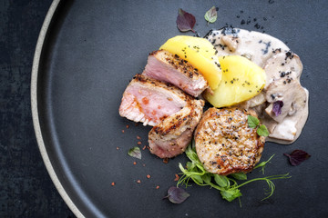 Fried pork fillet with boiled potatoes and mushrooms in cream sauce as top view on a plate with copy space left