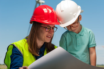 Cute young mother engineer in a red helmet and glasses shows her engineering plan to her talented...