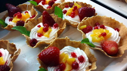Bowls of wafer with whipped cream and fruit on a white plate.