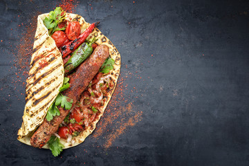 Traditionelles Adana Kebap mit Tomaten und Salat auf Fladenbrot  auf einem Board mit Textfreiraum rechts 