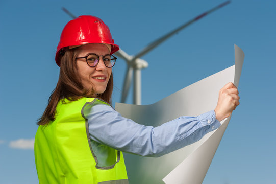 Charming young woman engineer looking at a plan of repair work on the background of a windmill