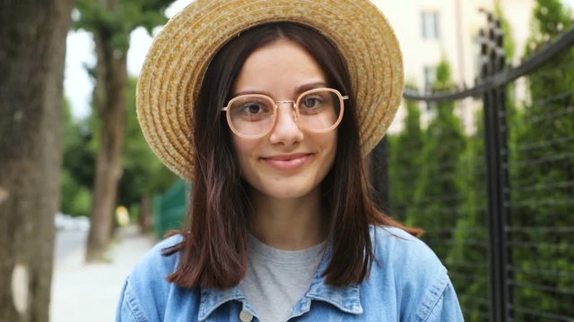 smiling attractive girl in sunglasses and straw hat walking with smiling face and looking at camera long brunette hair friendly happy emotions woman wearing trendy casual summer clothes summertime