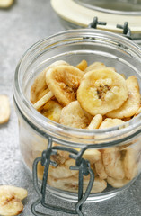 Homemade dried banana chips in a glass jar and fresh bananas.  Yellow fried fruit slices. Healthy sweet snack. Vegetarianism